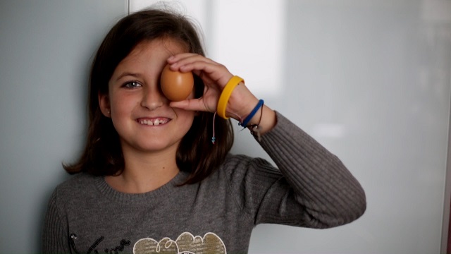 "Una niña sonriente mirando a la camara, sujetando un huevo con la mano izquierda, "